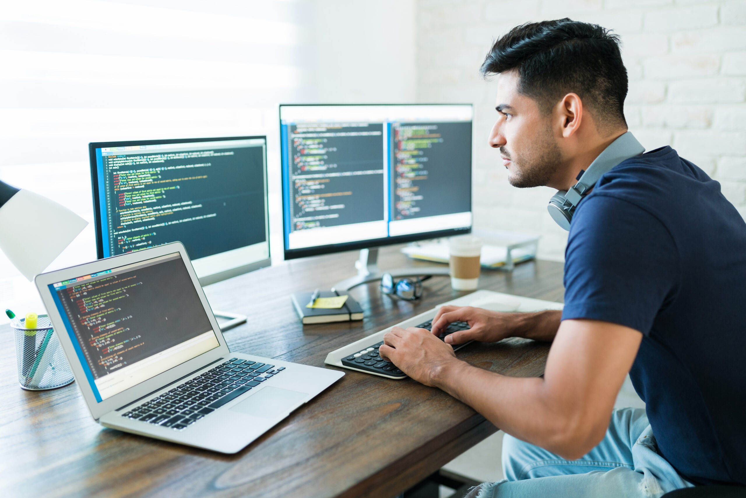 A web developer working on code across multiple monitors at a desk