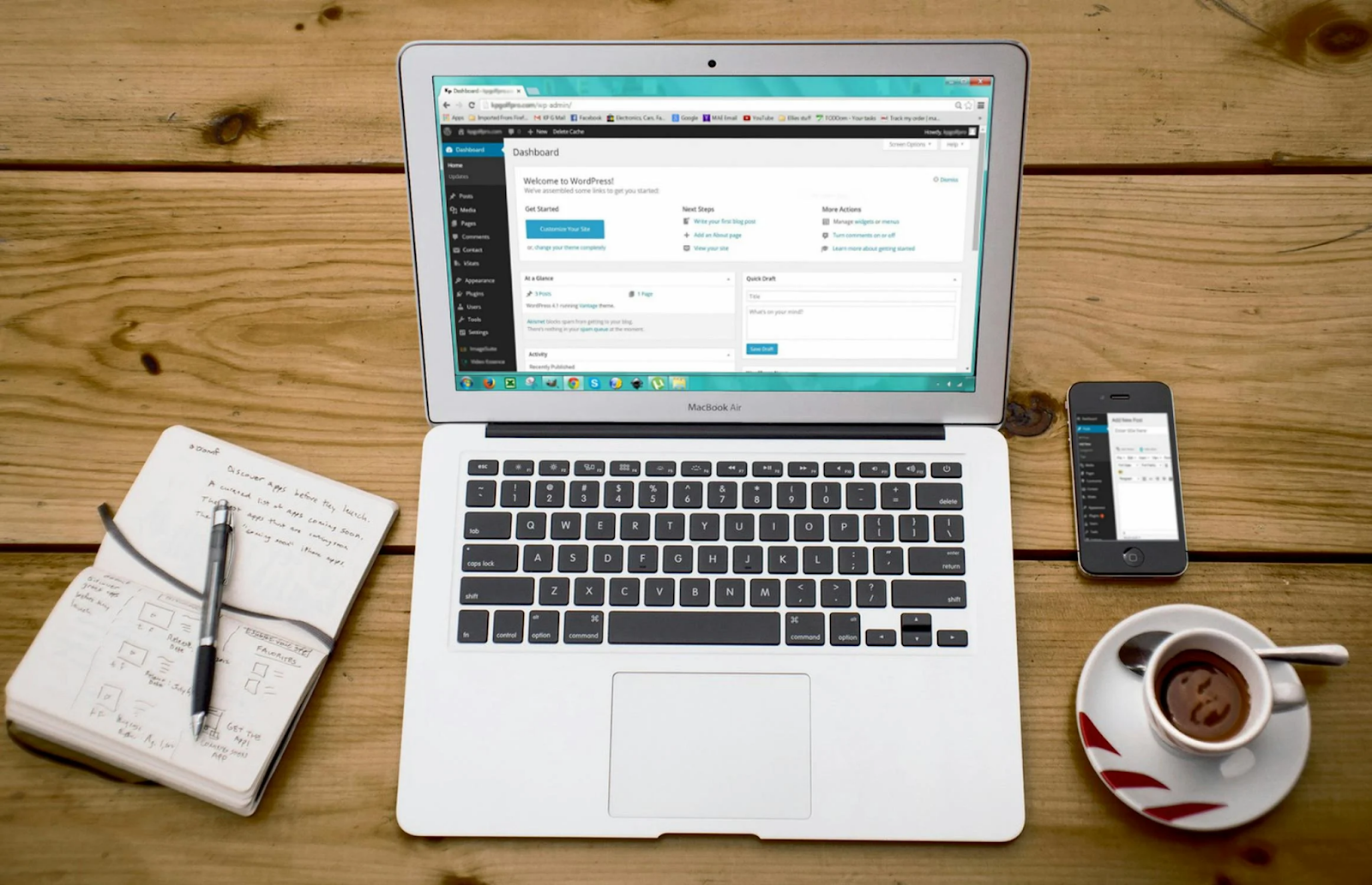 Turned-on Macbook Air Beside Black Phone, Cup of Tea, and Notebook on Brown Wooden Surface