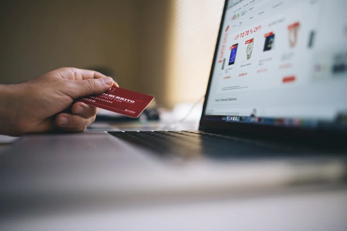 Person holding a red credit card while shopping online on a laptop