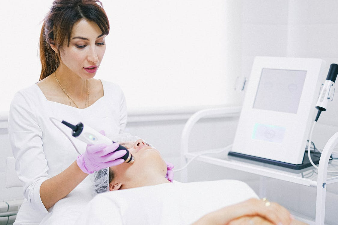 A Woman in White Shirt Lying on Bed while having a Facial Treatment